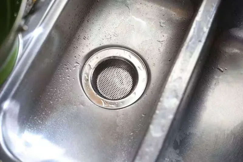 Pia de cozinha de inox molhada com ralo e escorredor de pia. Gotas de água na superfície