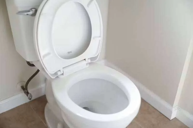 Vaso sanitário branco com a tampa aberta, mostrando o interior do vaso e a tubulação de água na parede
